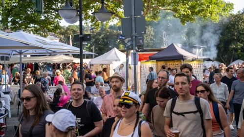 Die Menschen schlendern vorbei an Marktstände, einige mit Getränken in der Hand. Im Hintergrund: weiße Marktzelte und Verkaufsstände. 