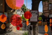 Bunte transparente Kreise hängen als Installation im Freien, auf einem steht eine handschriftliche Botschaft.