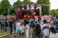 Ein Publikum steht auf einer Wiese vor einer beleuchteten Open-Air-Bühne mit Band.