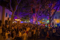 Eine belebte Altstadtstraße ist nachts mit bunten Lichtern, Lampions und vielen Besucherinnen und Besuchern gefüllt.