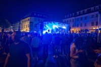 Eine nächtliche Open-Air-Bühne leuchtet blau, während davor viele Menschen auf dem Platz stehen.