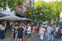 Eine belebte Altstadtstraße ist tagsüber mit vielen Besucherinnen und Besuchern sowie bunten Lampions geschmückt.