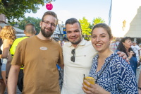 Drei Personen stehen lächelnd eng beieinander auf dem Stadtfest, eine Frau hält ein Getränk in der Hand.