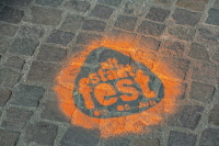 Ein orange leuchtendes Stadtfest-Logo ist auf das Kopfsteinpflaster projiziert.