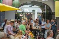Besucherinnen und Besucher sitzen und stehen unter Papierlampions an Tischen in einem Innenhof.
