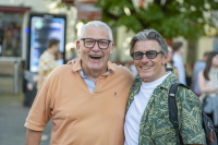 Zwei ältere Männer stehen lachend mit den Armen umeinander auf dem Stadtfest.