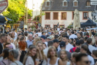 Eine belebte Altstadtgasse ist voller Menschen, im Hintergrund steht ein Gebäude mit der Aufschrift „Antiquariat“.