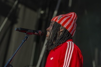 Ein Sänger mit roter Jacke und gestreifter Mütze singt seitlich in ein Bühnenmikrofon.