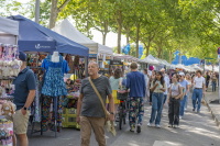 Menschen schlendern an Marktständen mit Kleidung, Accessoires und Spielwaren entlang.