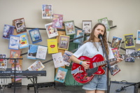 Eine Musikerin singt und spielt rote E-Gitarre vor einer Wand mit historischen Altstadtfest-Plakaten.