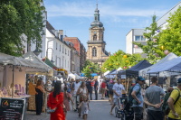 Blick auf Basilika, Altstadtfest Freitag, 3. Juli 2026 Eine Marktstraße mit vielen Ständen, Besucherinnen und Besuchern führt auf eine Kirche im Hintergrund zu.