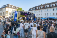 Publikum steht vor einer Bühne auf einem Platz bei einem Open-Air-Konzert.