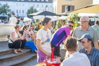 Menschen sitzen und stehen an Tischen am Markt in der Abendsonne.