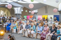 Menschen sitzen in einem geschmückten Innenhof mit Lampions vor einer Bühne.