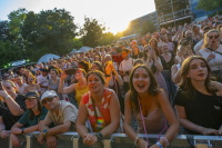 Dichtes Publikum steht bei Sonnenuntergang vor einer Bühne und schaut zum Konzert.