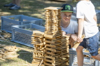 Zwei Kinder bauen im Freien einen hohen Turm aus Holzklötzen.