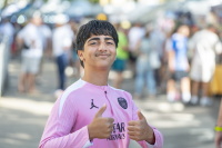 Jugendlicher in rosa Fußballtrikot zeigt mit beiden Händen Daumen hoch.