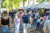 Menschen gehen zwischen Verkaufsständen auf einem sommerlichen Straßenfest.