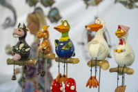 Bunte Keramikfiguren von Tieren sitzen auf Stangen an einem Marktstand.