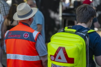 Zwei Johanniter-Einsatzkräfte stehen mit Warnweste und Notfallrucksack auf einem Festgelände.