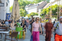 Menschen gehen und sitzen in einer belebten Gasse mit Gastronomie im Freien.