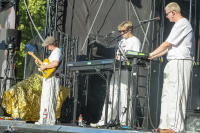 Drei Musiker in weißen Outfits spielen auf einer Bühne.