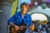 Ein Musiker in blauem Hemd spielt Gitarre auf einer Bühne.