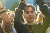 Nahaufnahme einer Person im Publikum mit erhobenen Armen bei Abendsonne.