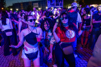 Drei junge Frauen tanzen nachts in blauem und violettem Licht vor einer Bühne.