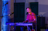 Musiker sitzt an einem Keyboard und singt in ein Mikrofon.