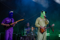 Drei maskierte Musiker spielen bei Nebel und grünem Licht auf einer Bühne.