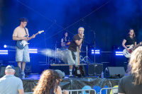 Band mit Gitarre, Bass, Schlagzeug und Gesang spielt auf einer blau beleuchteten Bühne.
