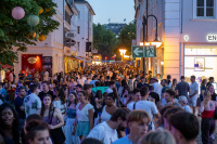 Viele Menschen stehen am Abend in einer belebten Altstadtgasse.