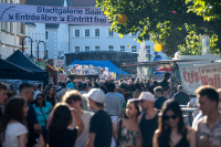 Menschenmenge auf einem sonnigen Markt unter dem Banner der Stadtgalerie Saarbrücken.